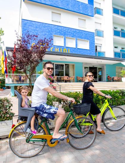 Famiglia in bicicletta davanti a un hotel moderno e colorato.