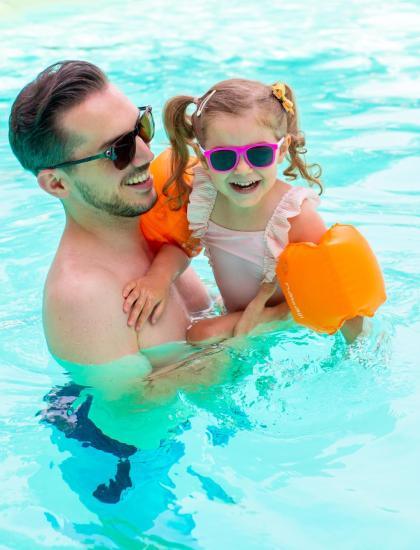 Papà e figlia sorridono in piscina con occhiali da sole.