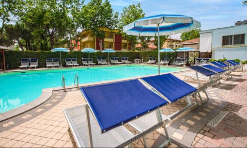 Outdoor pool with blue loungers and umbrellas, surrounded by trees.