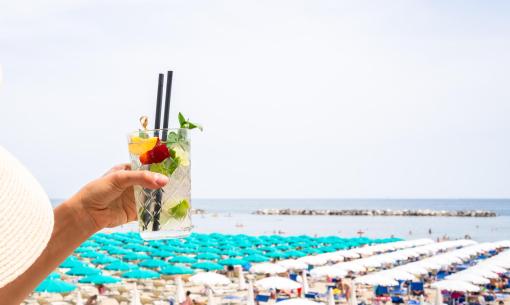 Cocktail in hand, crowded beach with colorful umbrellas.