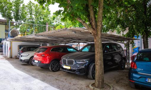 Überdachter Parkplatz mit Autos unter Bäumen.