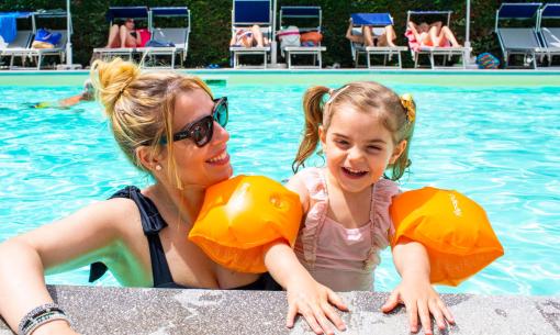 Glückliche Mutter und Tochter im Pool mit orangefarbenen Schwimmflügeln.