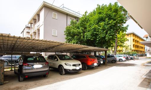 Parking couvert avec voitures devant des immeubles résidentiels.