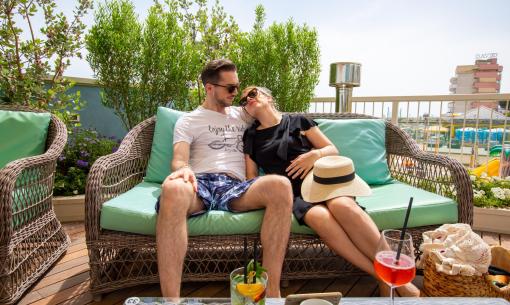 Couple détendu sur un canapé extérieur avec des boissons.