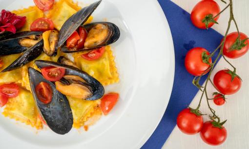 Raviolis aux moules et tomates cerises sur assiette blanche.