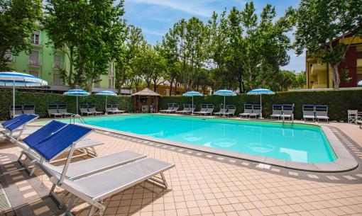 Outdoor pool with sun loungers and umbrellas, surrounded by trees.