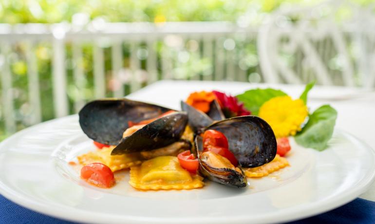 Piatto di ravioli con cozze e pomodorini, decorato con fiori.