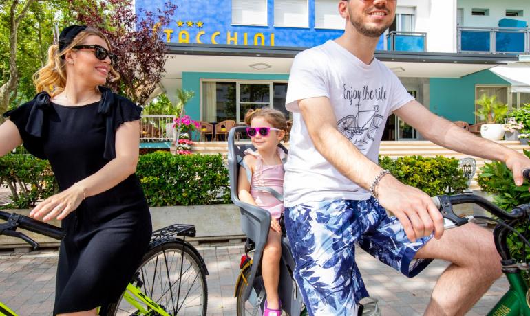 Familie radelt vor einem bunten Hotel.