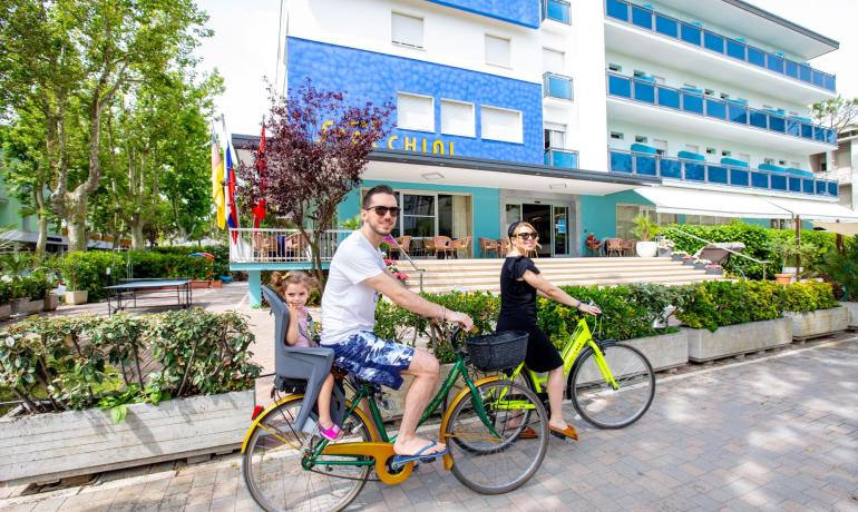 Famiglia in bicicletta davanti a un hotel moderno e colorato.