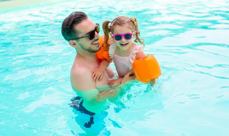 Papà e figlia sorridono in piscina con occhiali da sole.