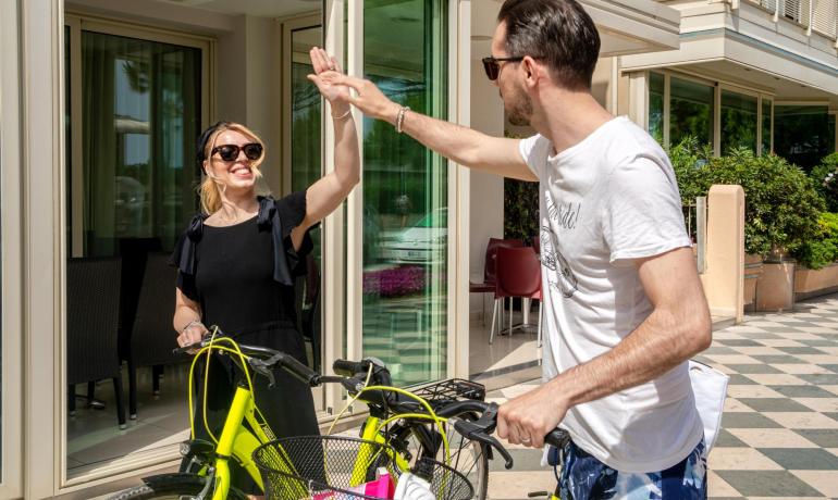 Two people on bikes high-five in front of a building.