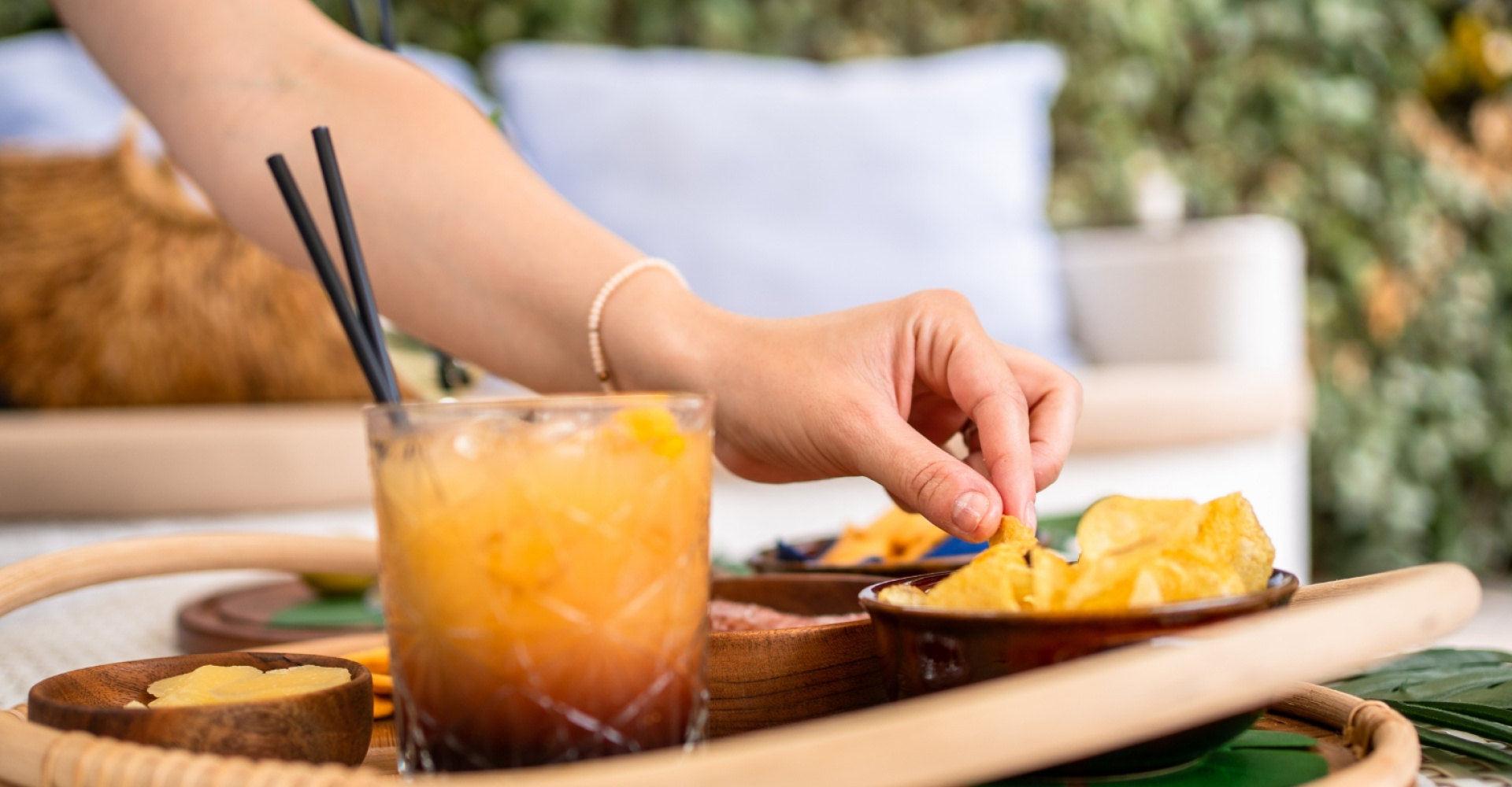 Mano prende patatine da un vassoio con bicchiere di cocktail e snack.