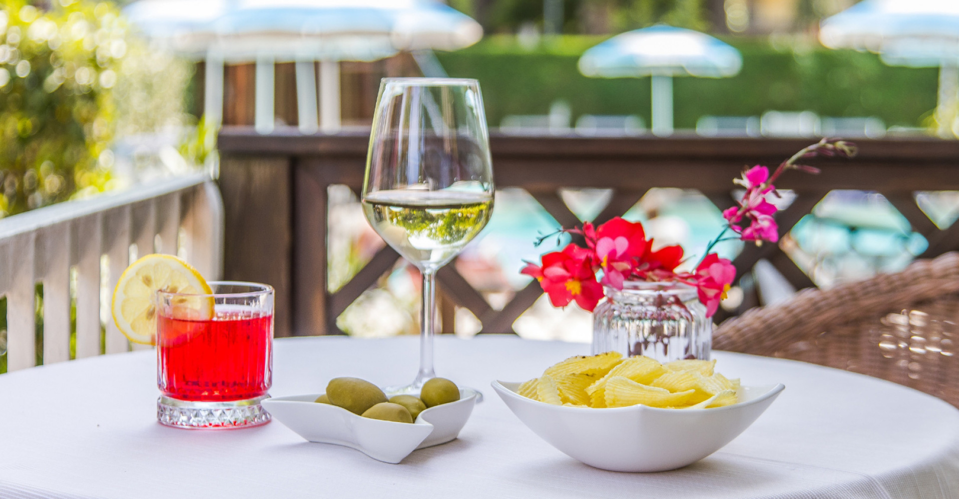 Tavolo con drink, vino bianco, olive, patatine e fiori, atmosfera estiva.