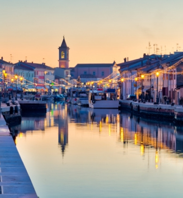 Canale al tramonto con luci e riflessi, atmosfera serena e festosa.