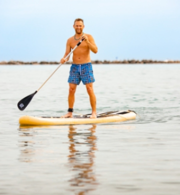 Uomo in costume, pagaia su tavola da SUP in mare calmo.