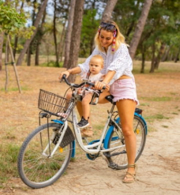 Donna con bambino su bicicletta in un parco alberato.