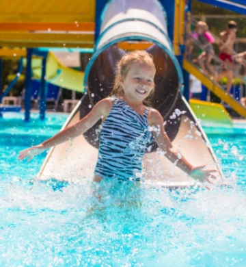 Bambina felice scivola in piscina, spruzzi d'acqua e divertimento estivo.