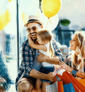 Famiglia felice con palloncini e borse della spesa, sorridono all'aperto.