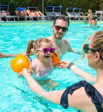 Famiglia felice si diverte in piscina con la bambina.