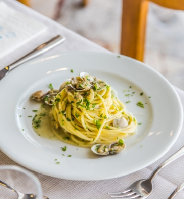 Spaghetti alle vongole con prezzemolo su piatto bianco.