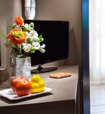 Fiori e frutta decorano un mobile con TV in una stanza luminosa.