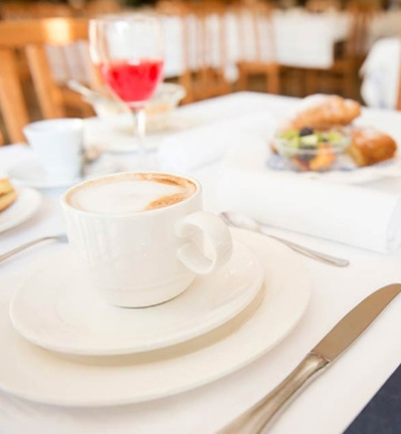 Colazione elegante con cappuccino, croissant e bevanda rossa su tavola apparecchiata.