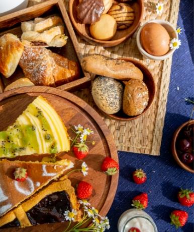 Colazione con dolci, frutta fresca e pane su tovaglia blu.