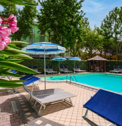 Piscina all'aperto con lettini e ombrelloni, circondata da alberi.