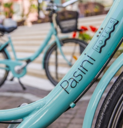 Bicicletta azzurra con logo Pasini Hotels, parcheggiata su stradina lastricata.