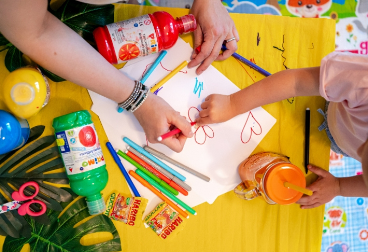 Bambino e adulto disegnano insieme con pastelli e colori su un tavolo colorato.