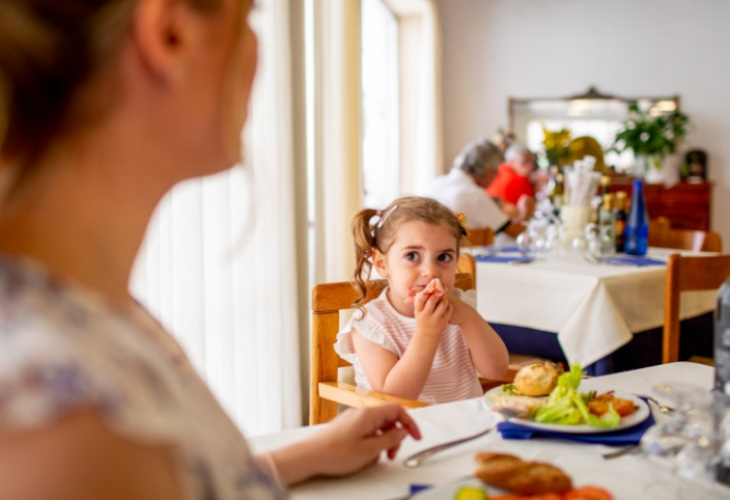 Bambina mangia a tavola con la famiglia in un ristorante luminoso.