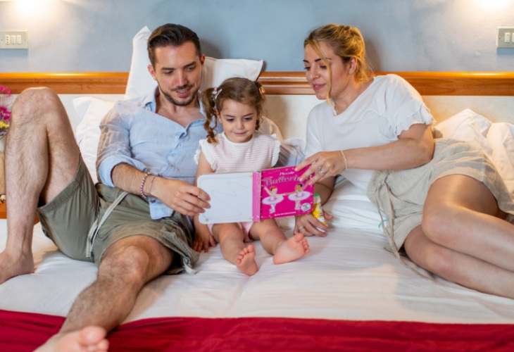 Famiglia sul letto legge un libro illustrato insieme alla bambina.