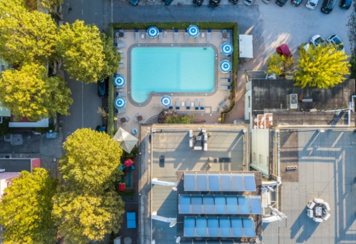 Vista aerea di una piscina circondata da lettini e ombrelloni blu e bianchi.