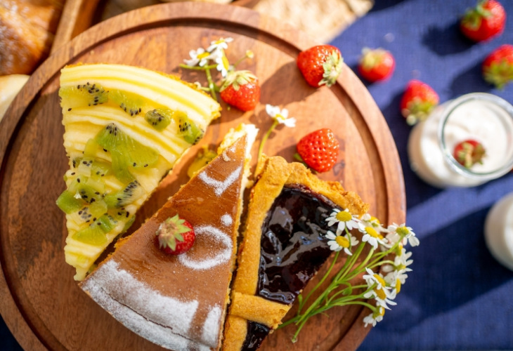 Due fette di torta con frutta e fiori su un piatto di legno.