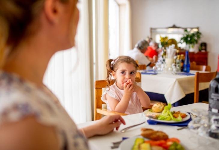 Bambina mangia a tavola con adulti in un ristorante, atmosfera familiare e accogliente.