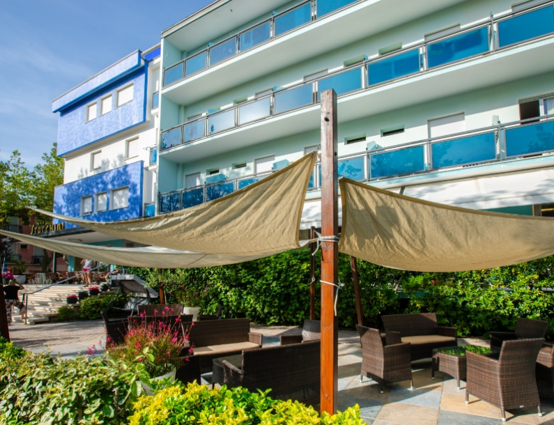 Hotel moderno con terrazza all'aperto, sedie in vimini e tende ombreggianti.