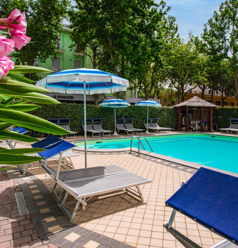 Piscina all'aperto con lettini e ombrelloni, circondata da alberi e cespugli verdi.