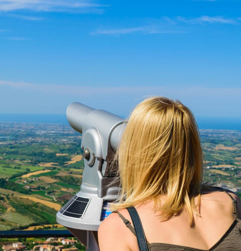 Donna osserva il panorama con un telescopio su una terrazza panoramica.