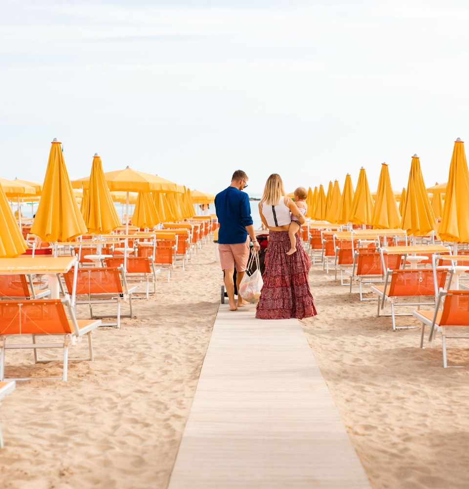 Famiglia cammina su una spiaggia con ombrelloni gialli e lettini arancioni.